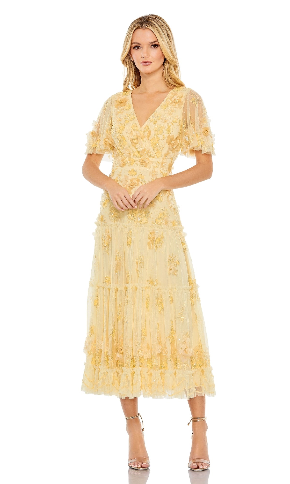 A woman wears the Mac Duggal 9207 A-Line Wedding Guest Dress, a light yellow floral tea-length dress with short sleeves and a V-neckline, ideal for wedding guests, standing against a white background.